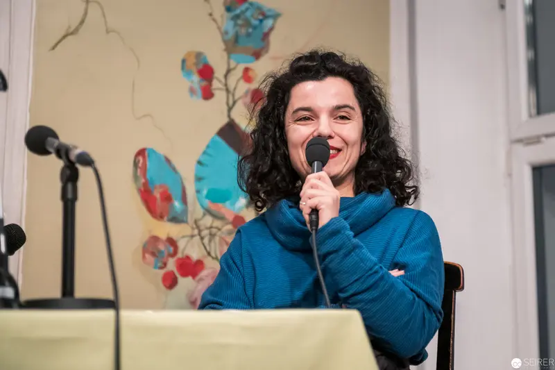Speaker in Blue Sweater Performing at Community Event with Floral Backdrop