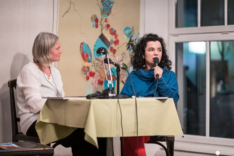 Two Women Engaged in Public Dialogue at Seated Panel Discussion