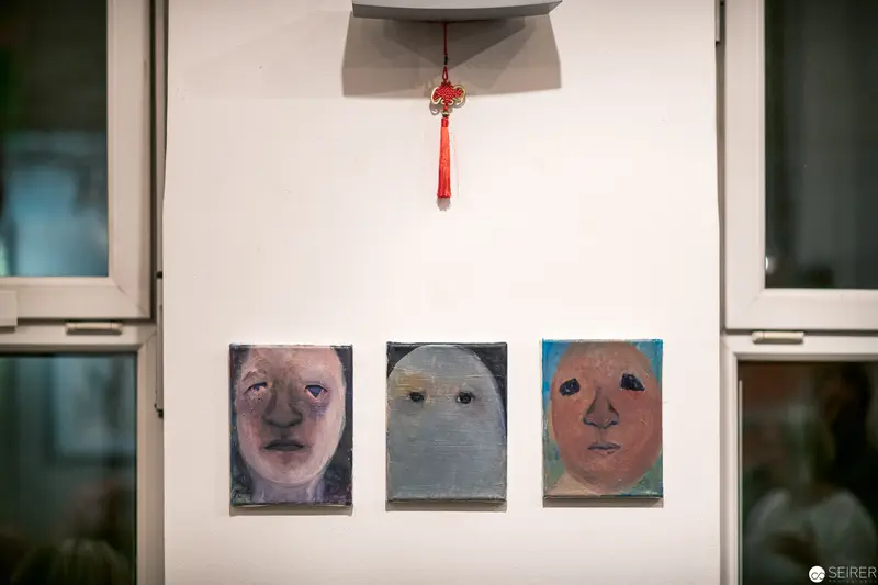 Three Distorted Portraits Hanging Below Decorative Red Tassel