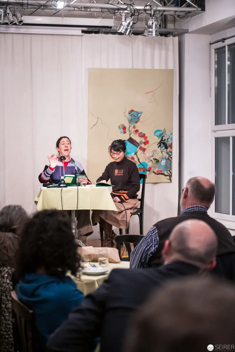 Two Performers at Literary Reading with Audience in Intimate Gallery Setting