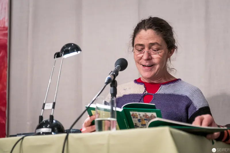 Woman Reading at Microphone During Literary Event in Colorful Sweater