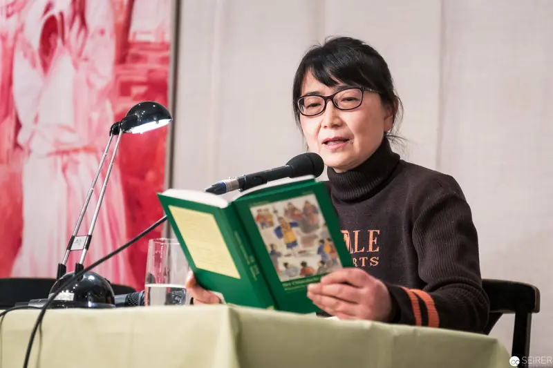 Writer Delivers Public Reading at Literary Event with Microphone and Green Book