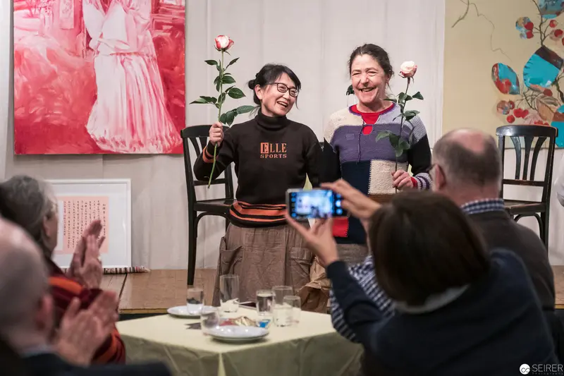 Two Women Sharing Roses During Intimate Gallery Reception