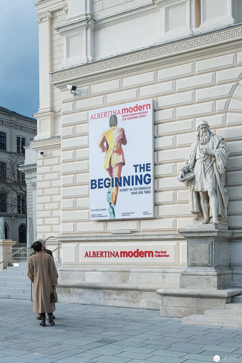 Albertina Modern's Exhibition Poster Displayed Beside Classical Statue in Urban Setting
