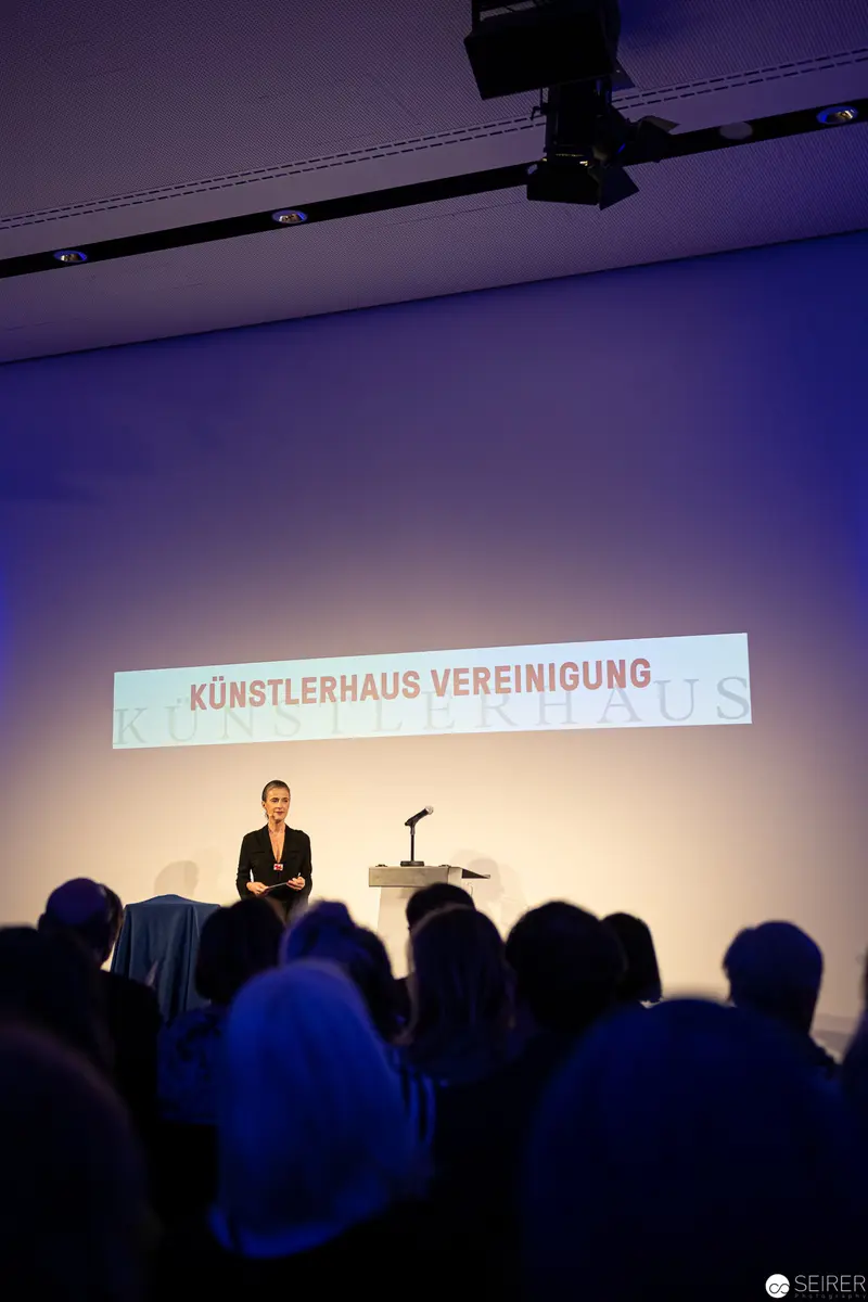 Künstlerhaus Vereinigung Wien Reopening: Speaker Addresses Audience in Blue-Lit Venue