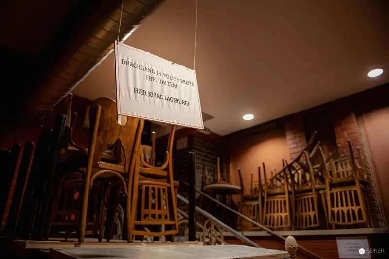 Suspended Sign Above Stacked Wooden Chairs in Empty Interior Space