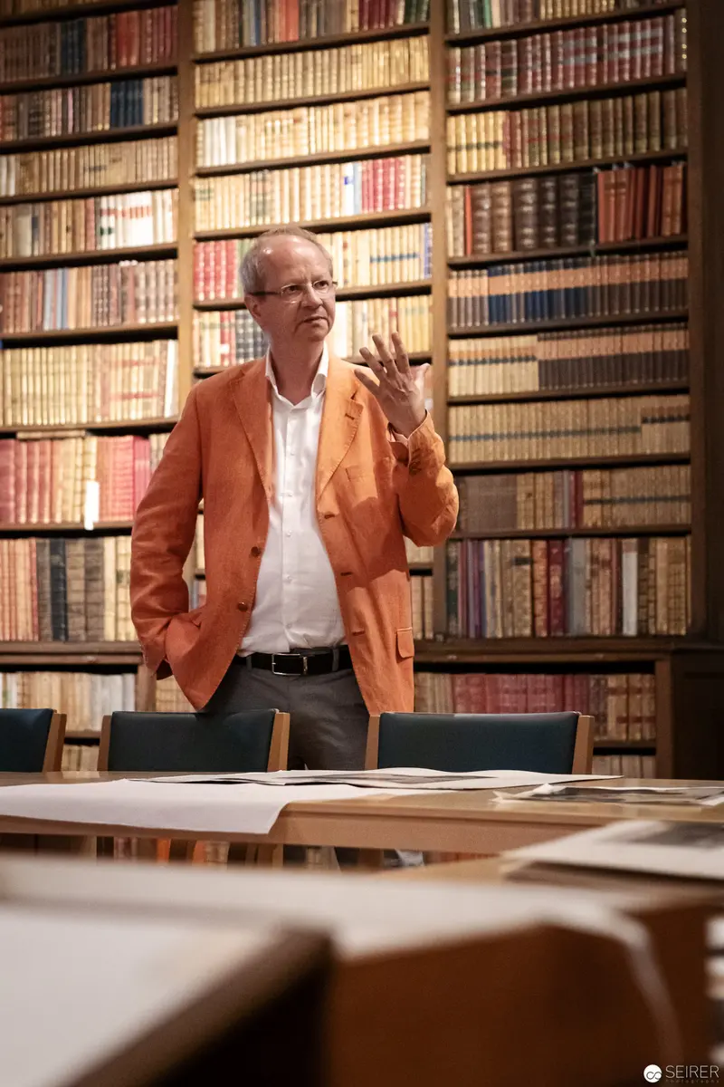 Scholarly Researcher in Orange Jacket Examining Rare Book Collection