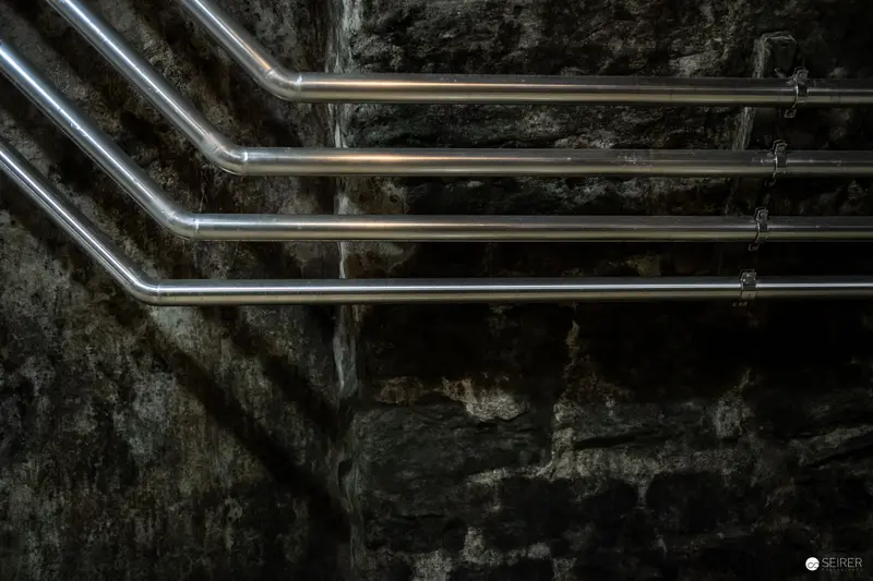 Industrial Metallic Pipes Against Dark Stone Wall in Monochromatic Study