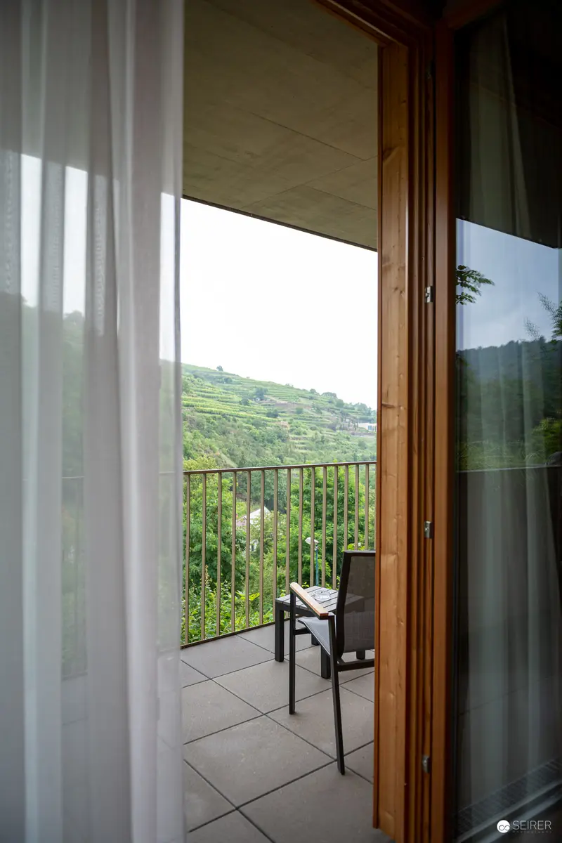 Balcony View of Verdant Hillside Landscape Through Translucent Curtains