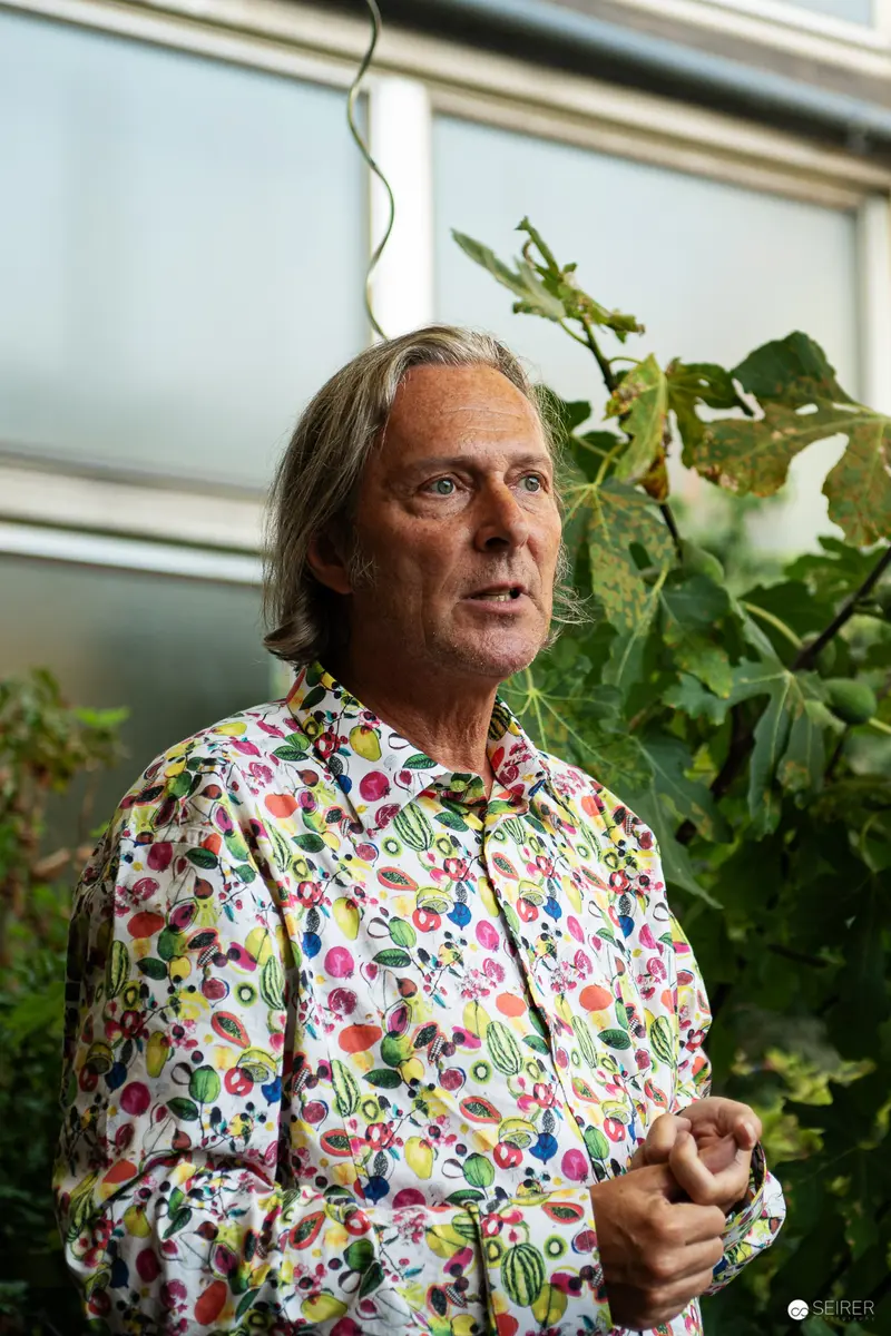 Gegenbauer Artisan in Vibrant Floral Shirt Amidst Greenhouse Foliage