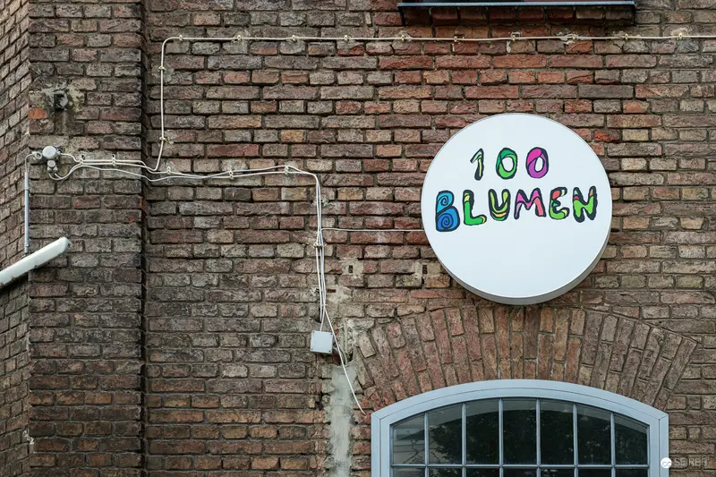 "100 Blumen" Signage on Weathered Brick Wall with Industrial Electrical Conduit