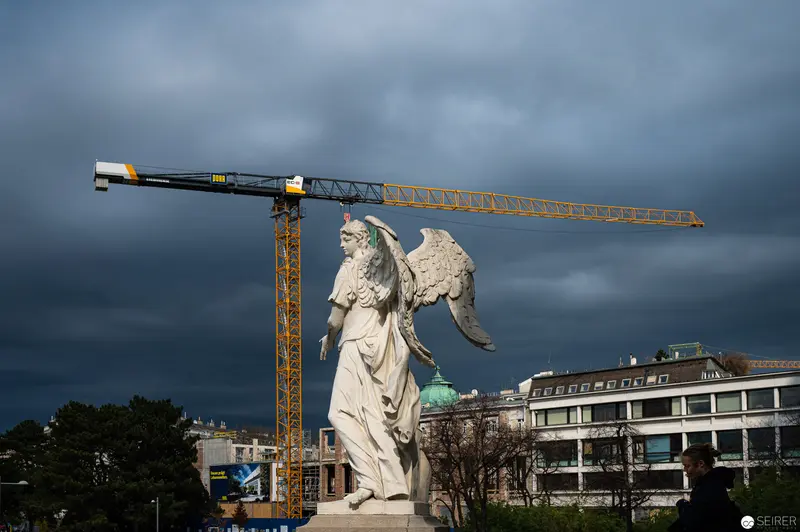 Angelic Statue Contrasts with Construction Crane in Brooding Urban Landscape