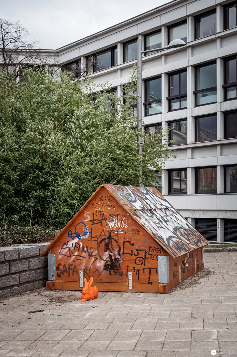 Graffitied Wooden Shelter Adjacent to Modernist Office Building