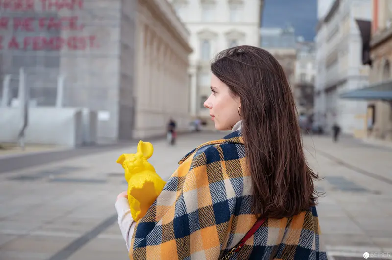 Woman in Yellow Gloves and Plaid Coat Observing Urban Streetscape