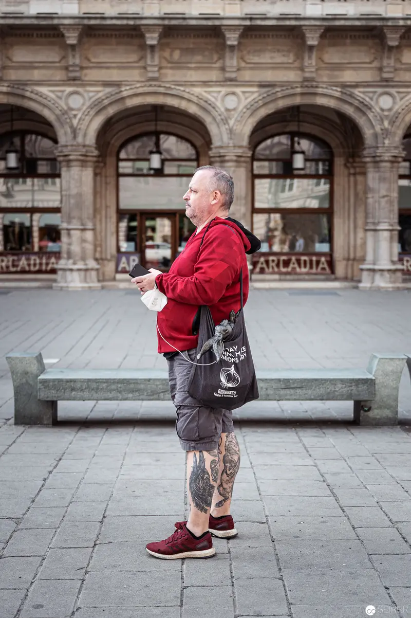 Standing Solitary in Urban Architecture: Red-Clad Figure with Elaborate Tattoos