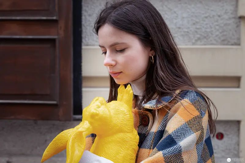 Young Woman in Plaid Contemplating Bright Yellow Stylized Animal Sculpture