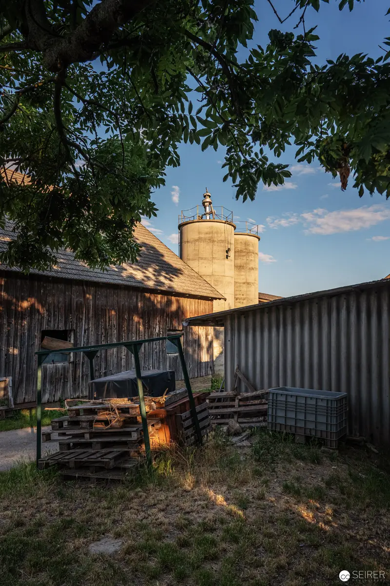 Rural Twilight: Farm Machinery Near Grain Silos at Golden Hour