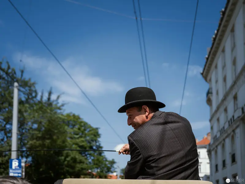 Elderly Gentleman in Bowler Hat at Urban Intersection under Power Lines
