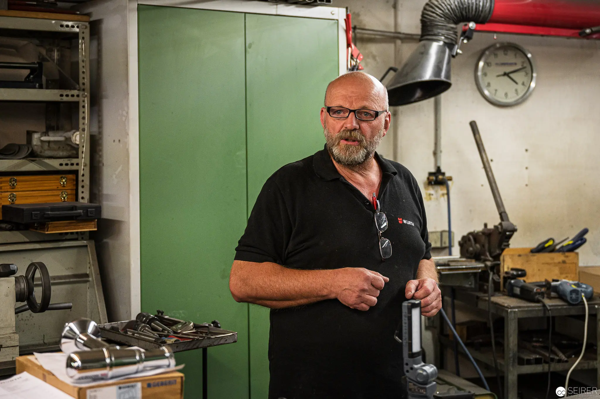 Workshop Craftsman in Black Polo Standing Amid Mechanical Tools and Equipment
