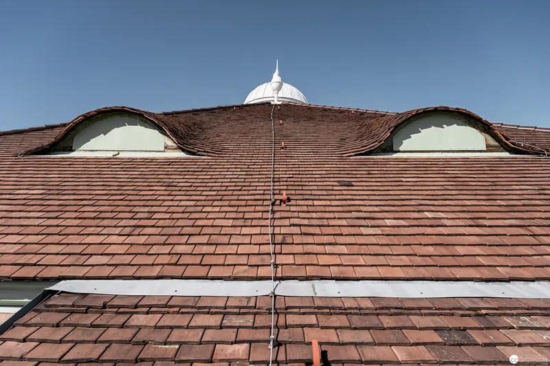 Terracotta-Tiled Roof with Curved Dormers and White Dome Against Blue Sky