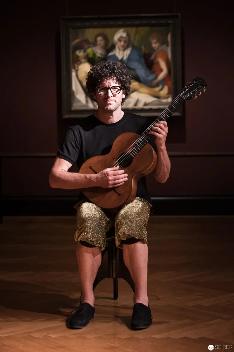 Performance Ganymed: Curly-Haired Guitarist in Ornate Museum Setting