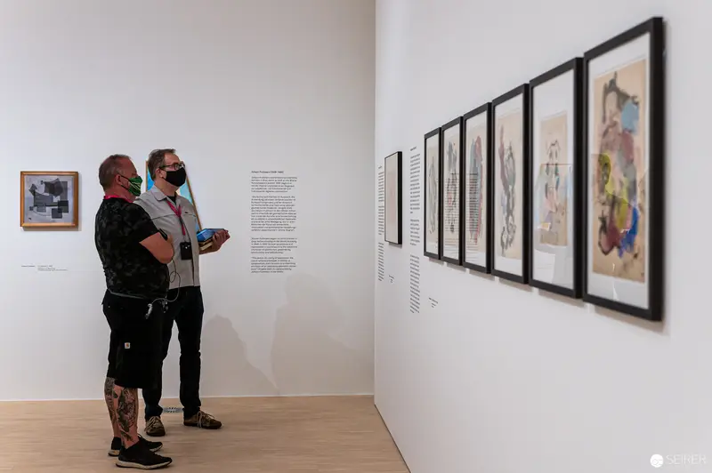 Two Visitors Examining Framed Artworks at Landesgalerie Niederösterreich Exhibition