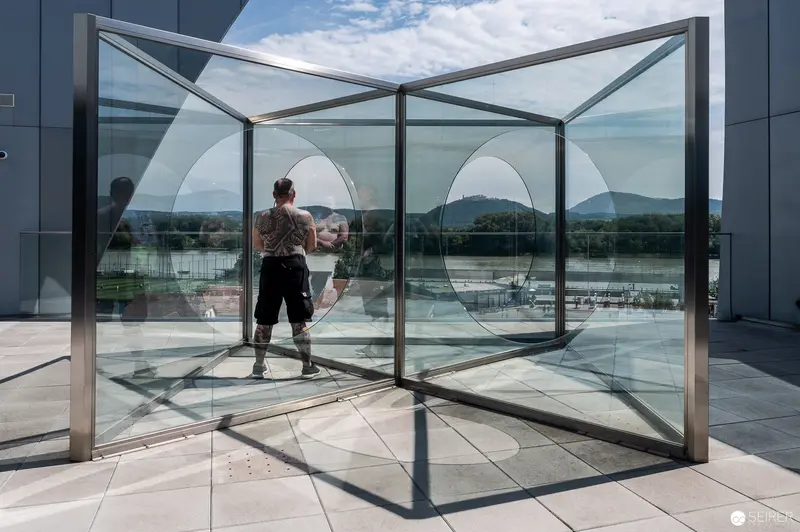 Translucent Geometric Glass Pavilion with Reflective Figure at Landesgalerie Niederösterreich