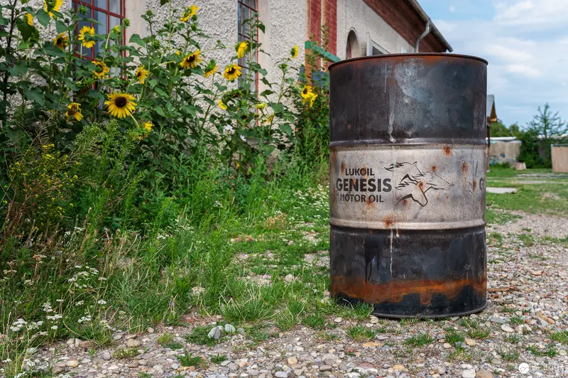Rusted Lukoil Genesis Motor Oil Barrel Amid Wildflowers and Weathered Building