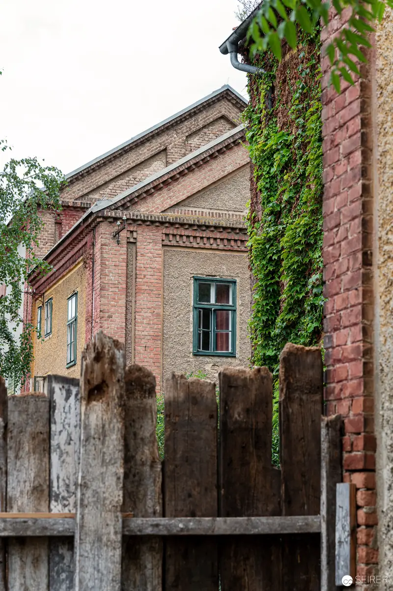 Ivy-Covered Brick Building with Weathered Wooden Fence in Rural Setting