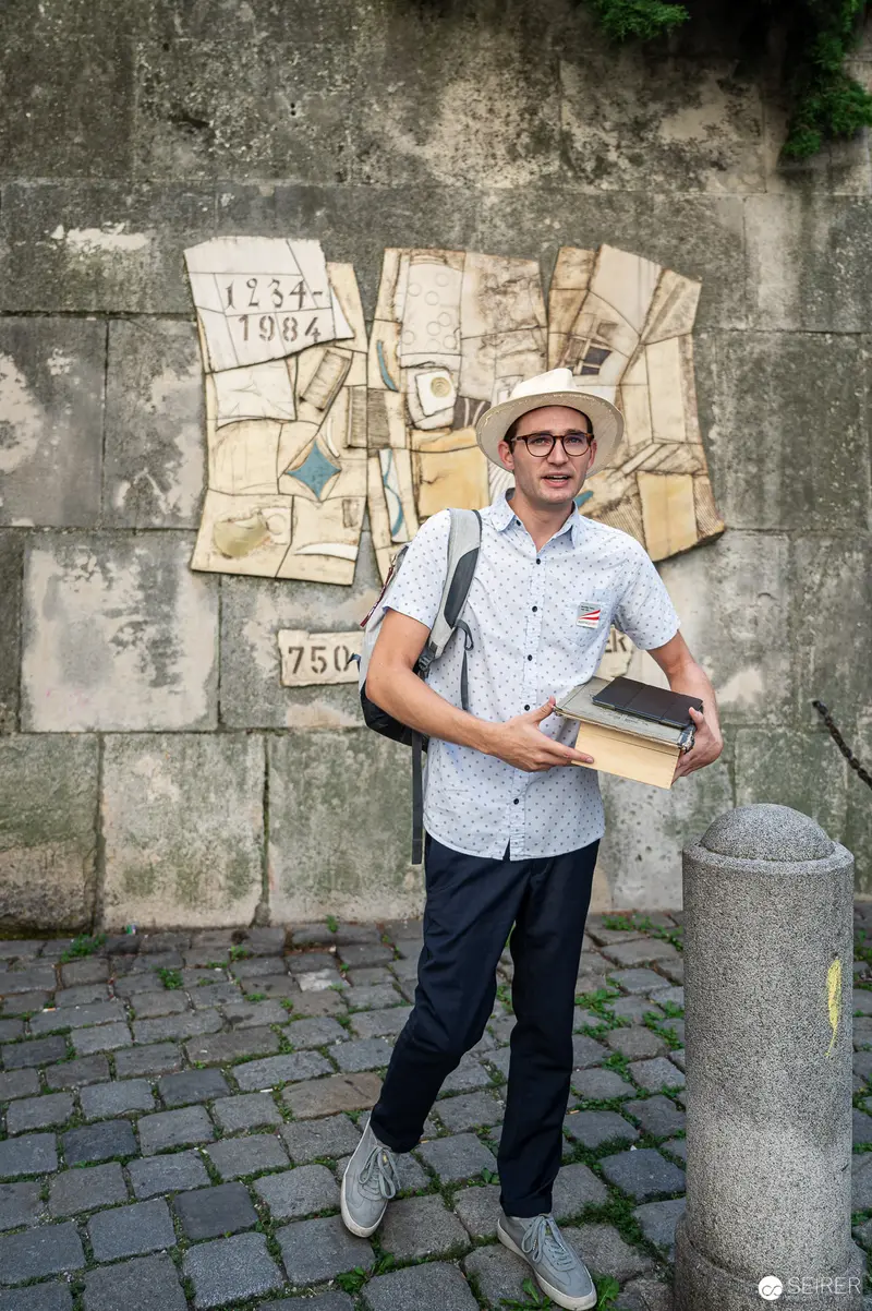 Scholarly Figure with Archival Materials Against Urban Textured Wall Background
