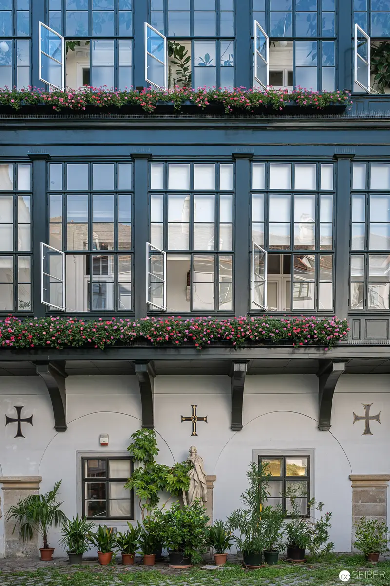 Baroque Architectural Facade with Floral Window Boxes and Religious Symbolism