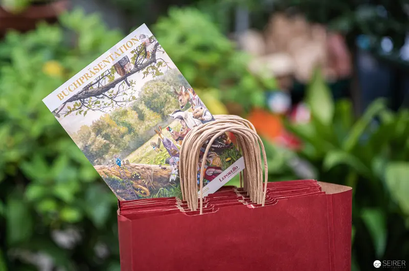 Book Reading at Deutschordenshaus: Illustrated Book and Red Bag in Garden Setting