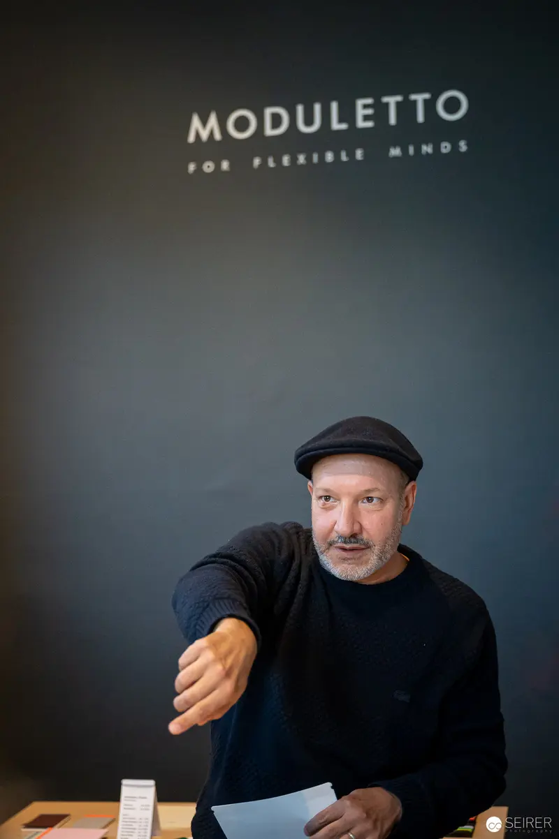 Moduletto Design Week Participant Gestures Thoughtfully at Branding Display