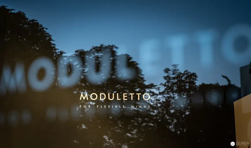 Moduletto Design Brand Concept with Reflective Typography and Atmospheric Urban Background