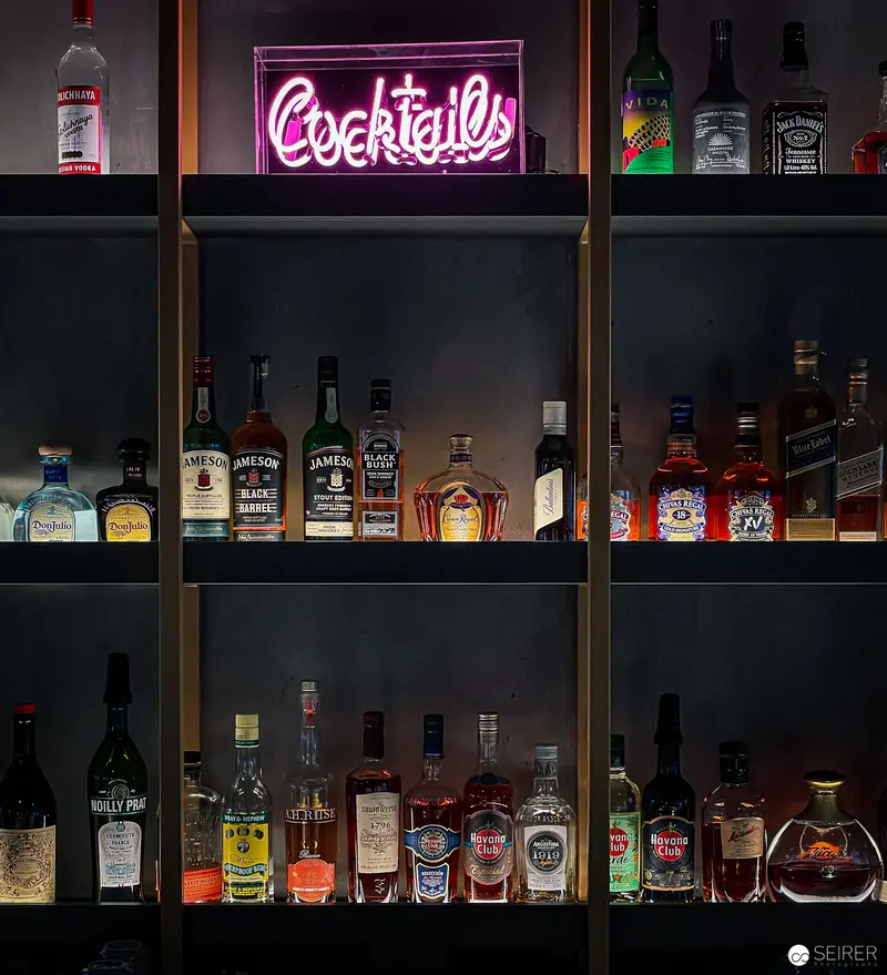 Neon Cocktails Sign Illuminating Extensive Liquor Collection on Dark Shelves