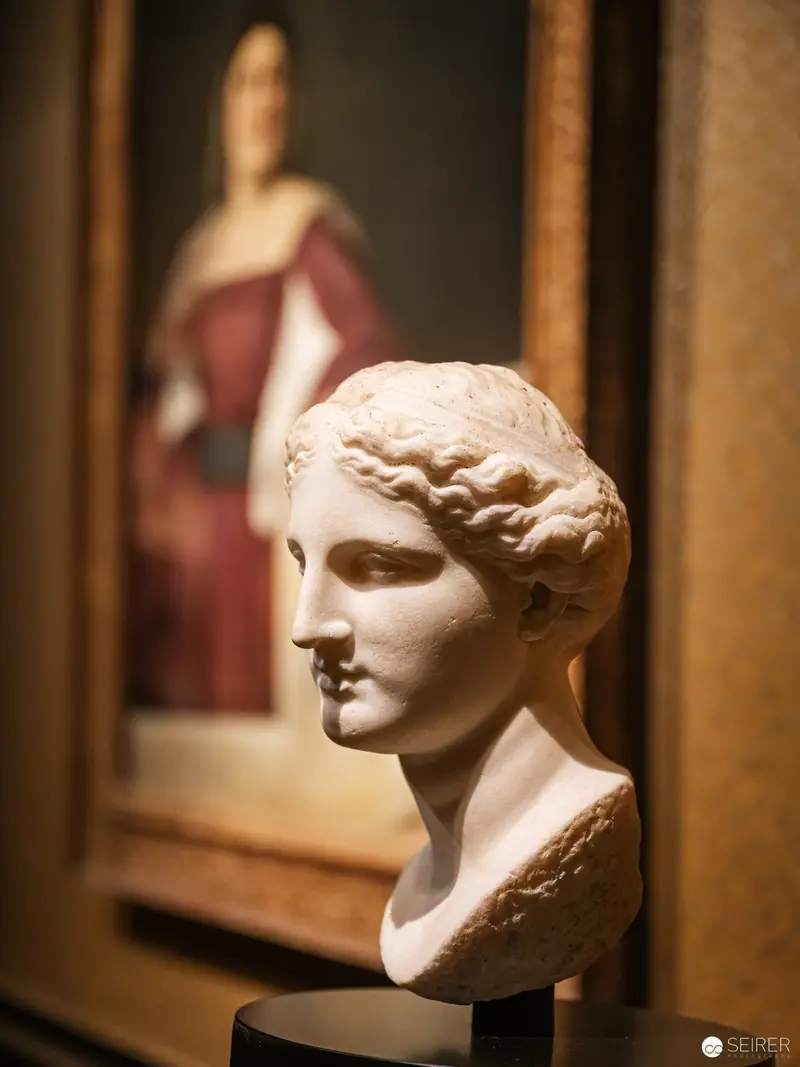 Marble Bust of Classical Figure with Blurred Red-Robed Background in Museum Display