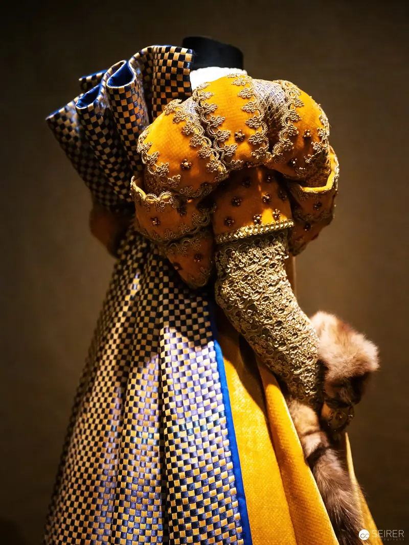 Intricately Draped Figure in Textured Yellow and Checkered Garments