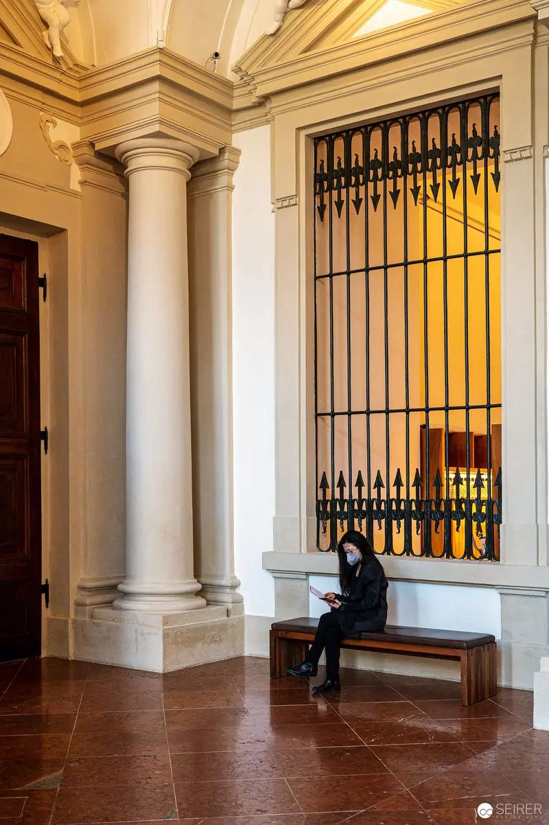 Solitary Figure in Neoclassical Interior with Architectural Columns and Iron Gate