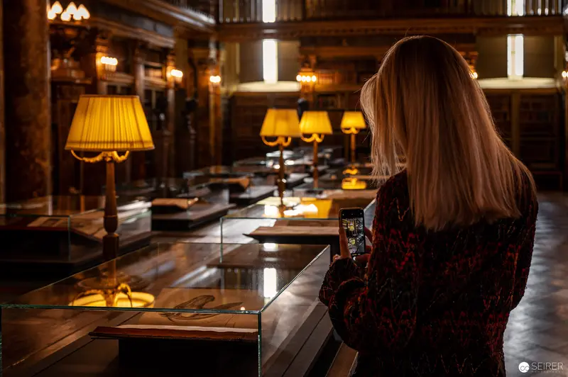 Scholarly Researcher Examining Illuminated Display in Elegant Archival Reading Room