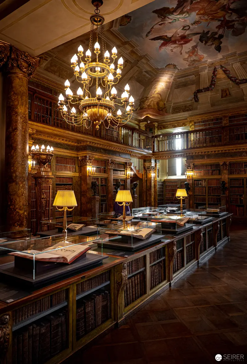 Ornate Historical Library Interior with Elaborate Chandelier and Illuminated Manuscript Display