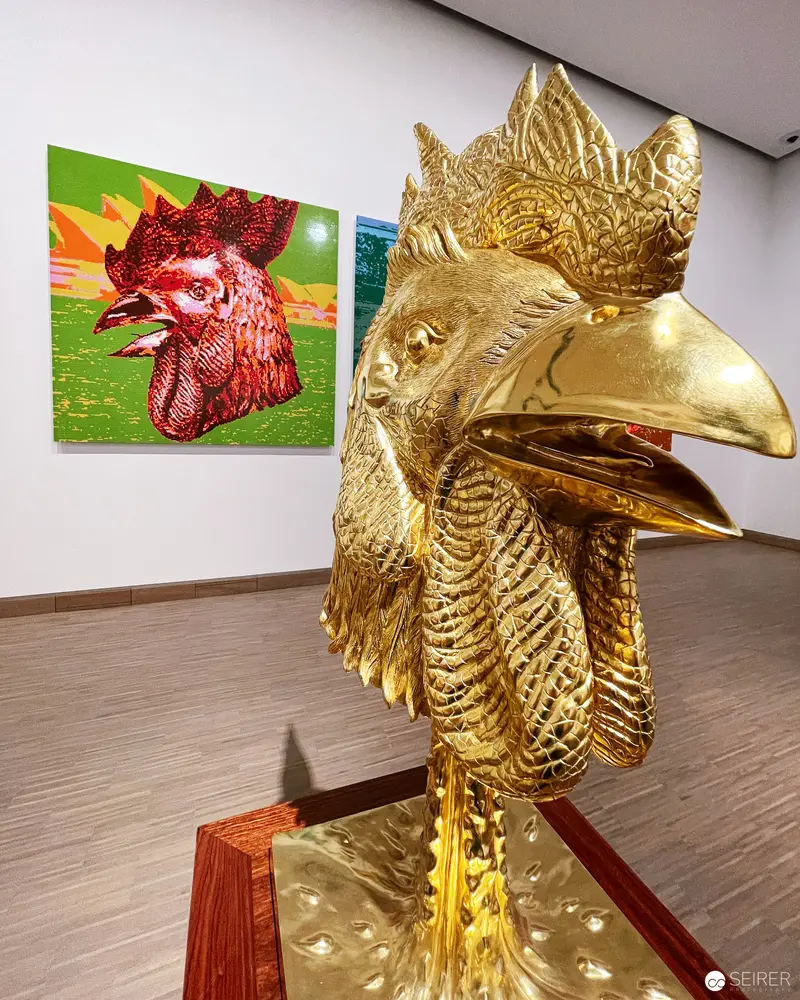 Golden Rooster Sculpture Juxtaposed with Rooster Painting in Gallery Setting