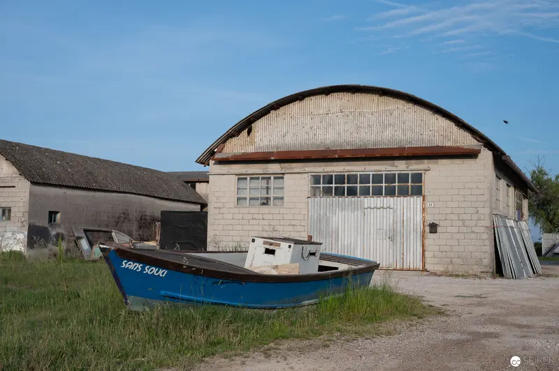Blue Fishing Boat Resting by Industrial Hangar in Coastal Landscape