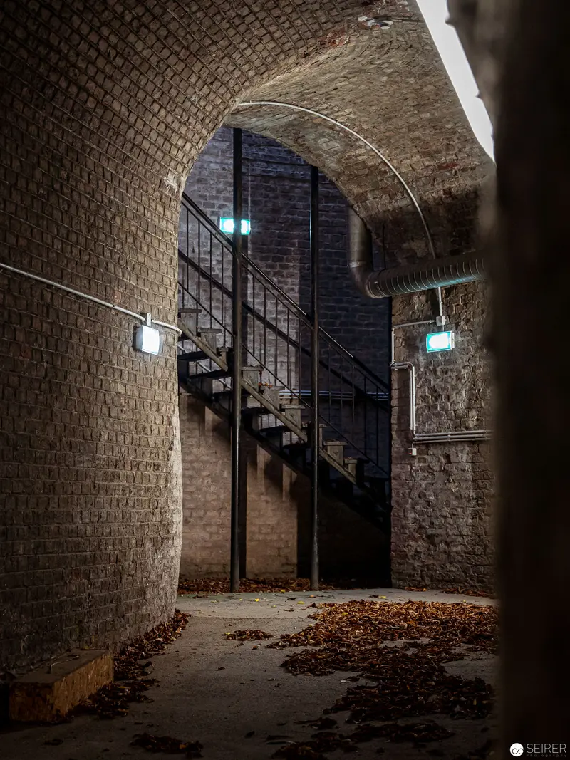 Vaulted Brick Passage with Metallic Staircase and Scattered Autumn Leaves