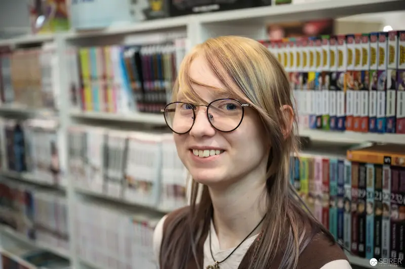 Blonde Librarian Smiling Amid Colorful Book Shelves at Comic Convention