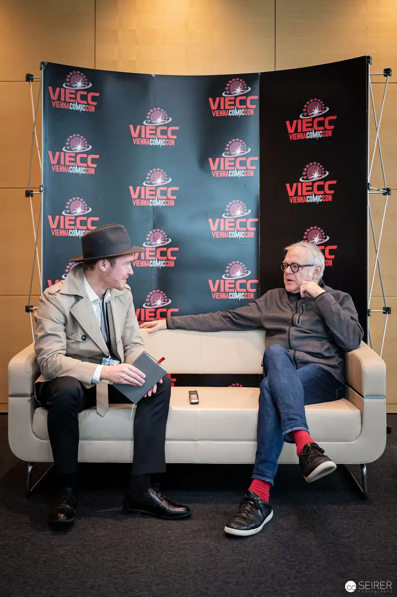 Vienna ComicCon Interview: Two Men on White Sofa with VIECC Backdrop