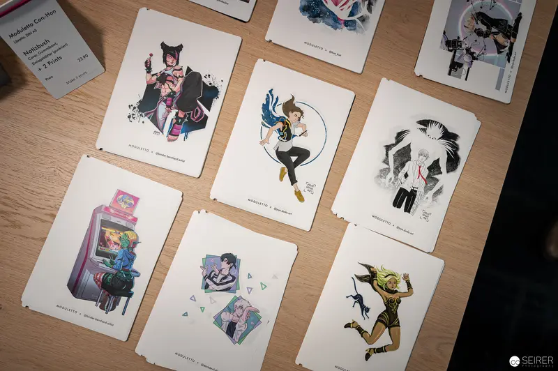 Illustrated Character Prints Displayed on Wooden Surface at Art Exhibition