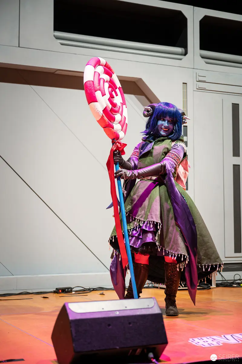 Cosplayer in Vibrant Purple and Green Costume Wielding Oversized Prop Staff at VIECC