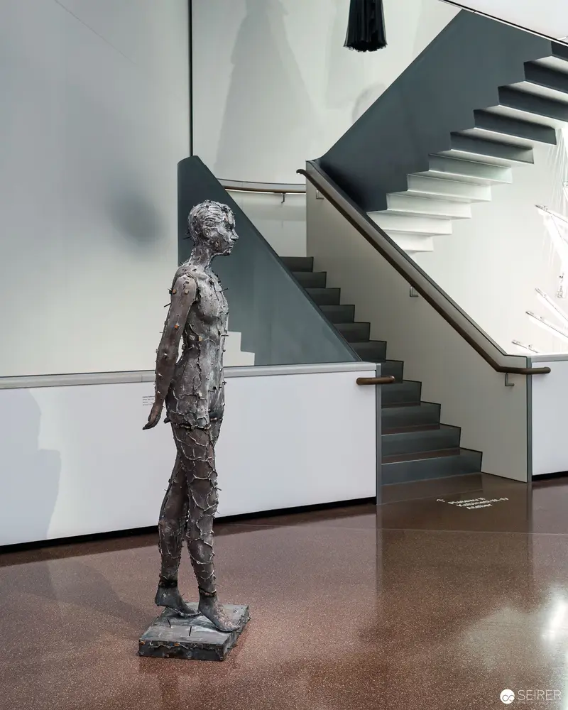 Textured Humanoid Sculpture in Minimalist Interior with Floating Staircase