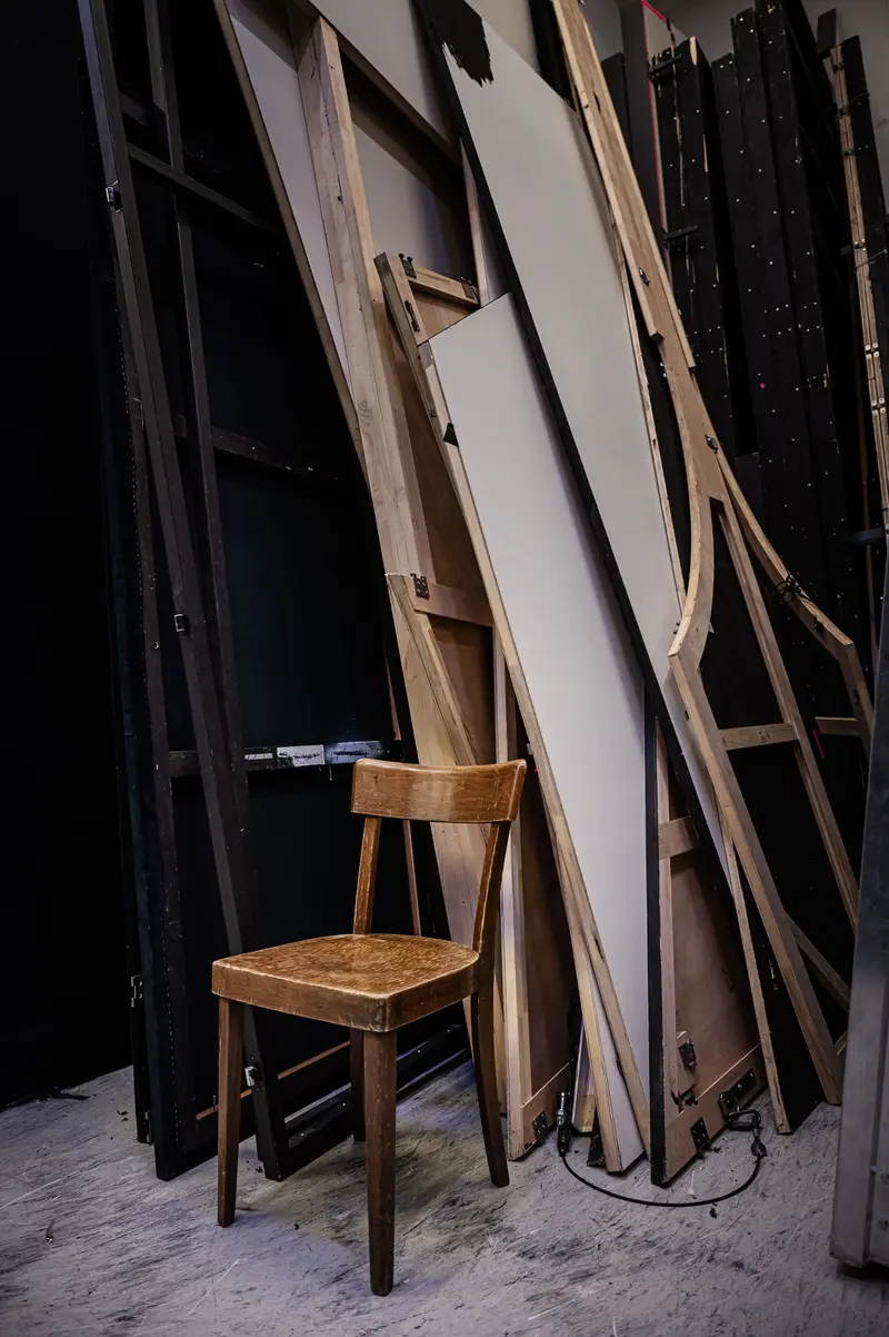 Wooden Chair Amid Stacked Panels in Dark Dramatic Studio Setting