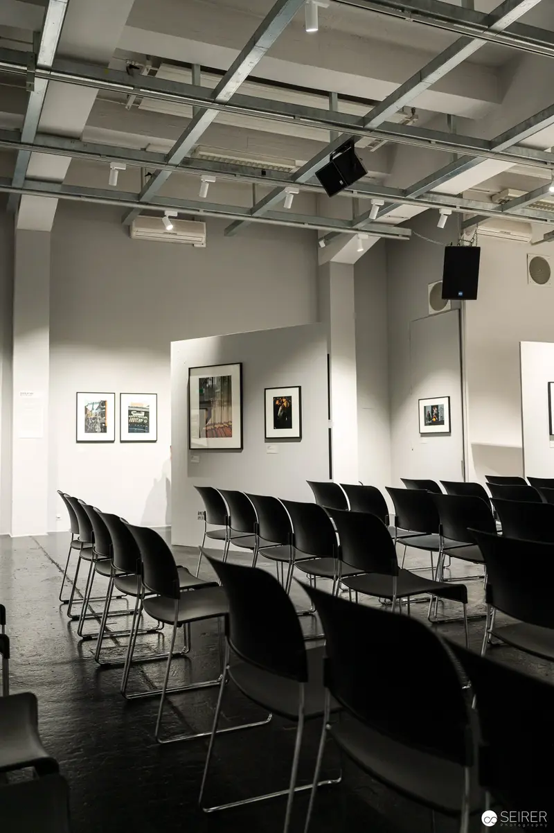 Empty Gallery Space with Black Chairs and Framed Photographs on White Walls